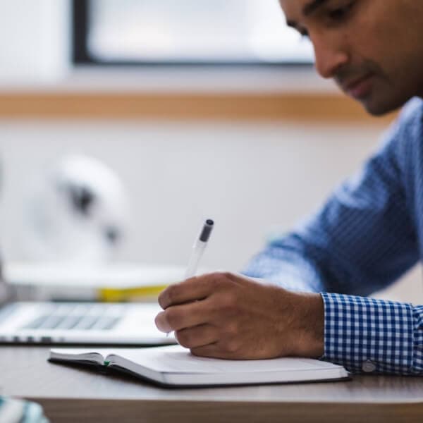 Man sitting at a desk, writing in a notebook, focused and productive.